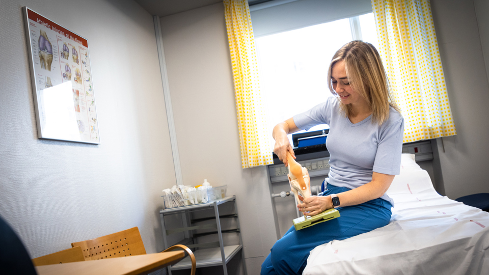 Kamilla Dessau sidder på en briks og holder en kopi af et knæ.