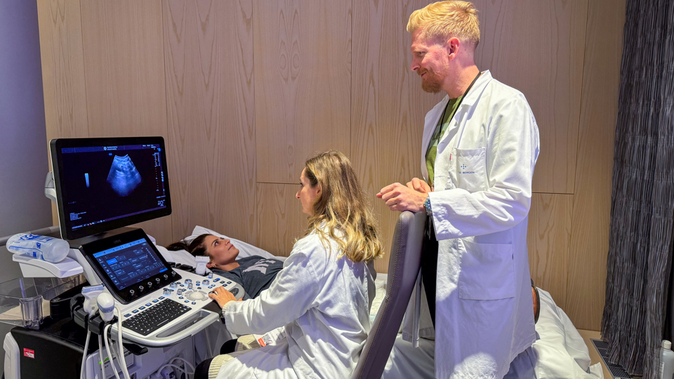 Kvinder bruger tarmultralyds-teknikken på kursus, mens mand står bagved og kigger på.
