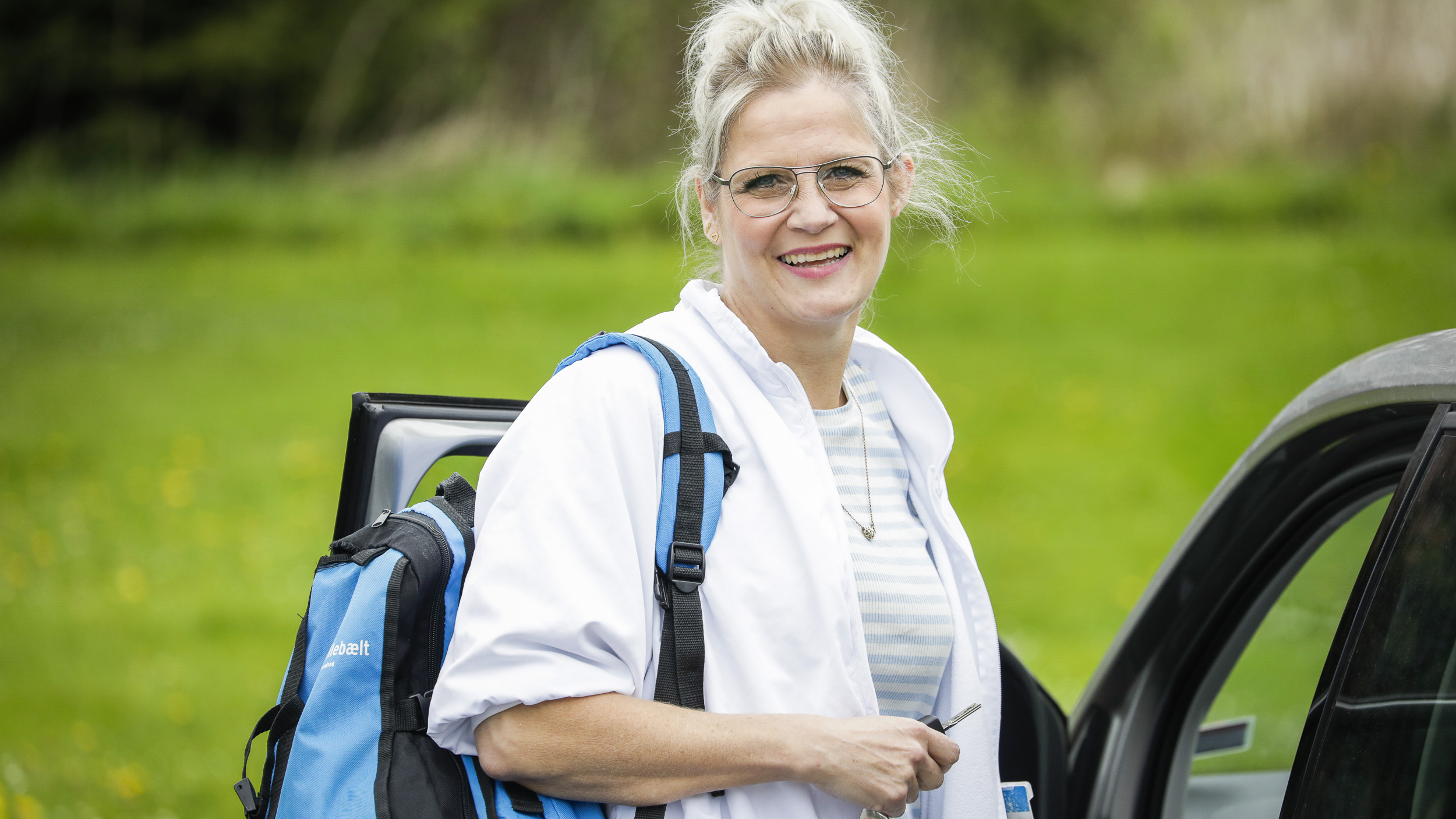 Smilende sygeplejerske står ved sin bil