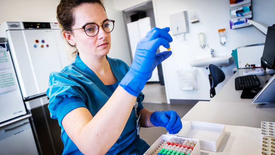 Læge undersøger prøveglas med blå handske på sin hånd.