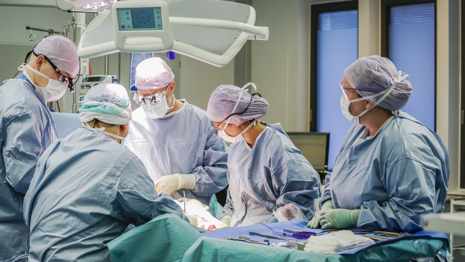 Fem læge og sygeplejersker i færd med at operere en patient