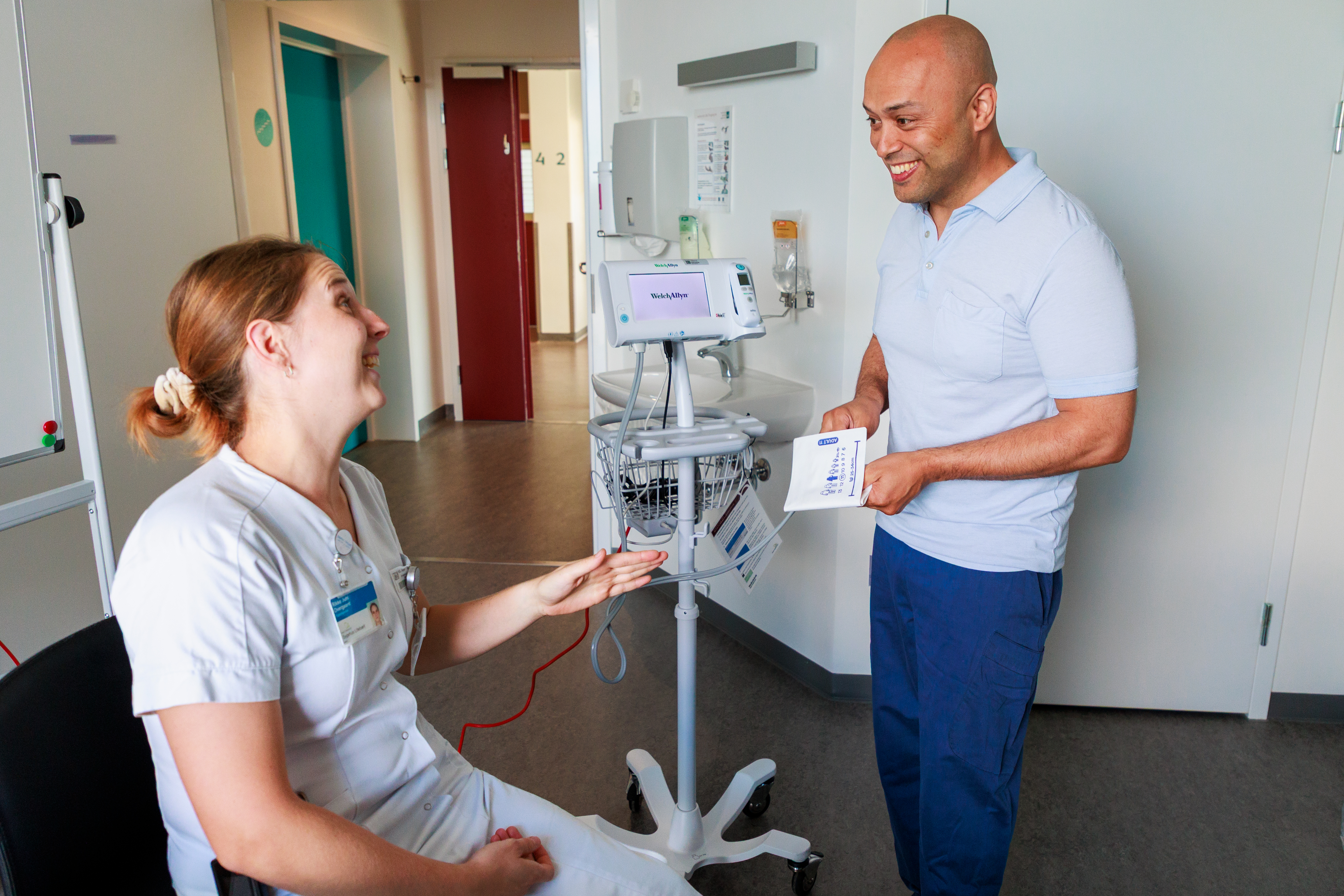 Kvindelig sygeplejerske og mandlig sygeplejerske taler smilende sammen på sygehusstue