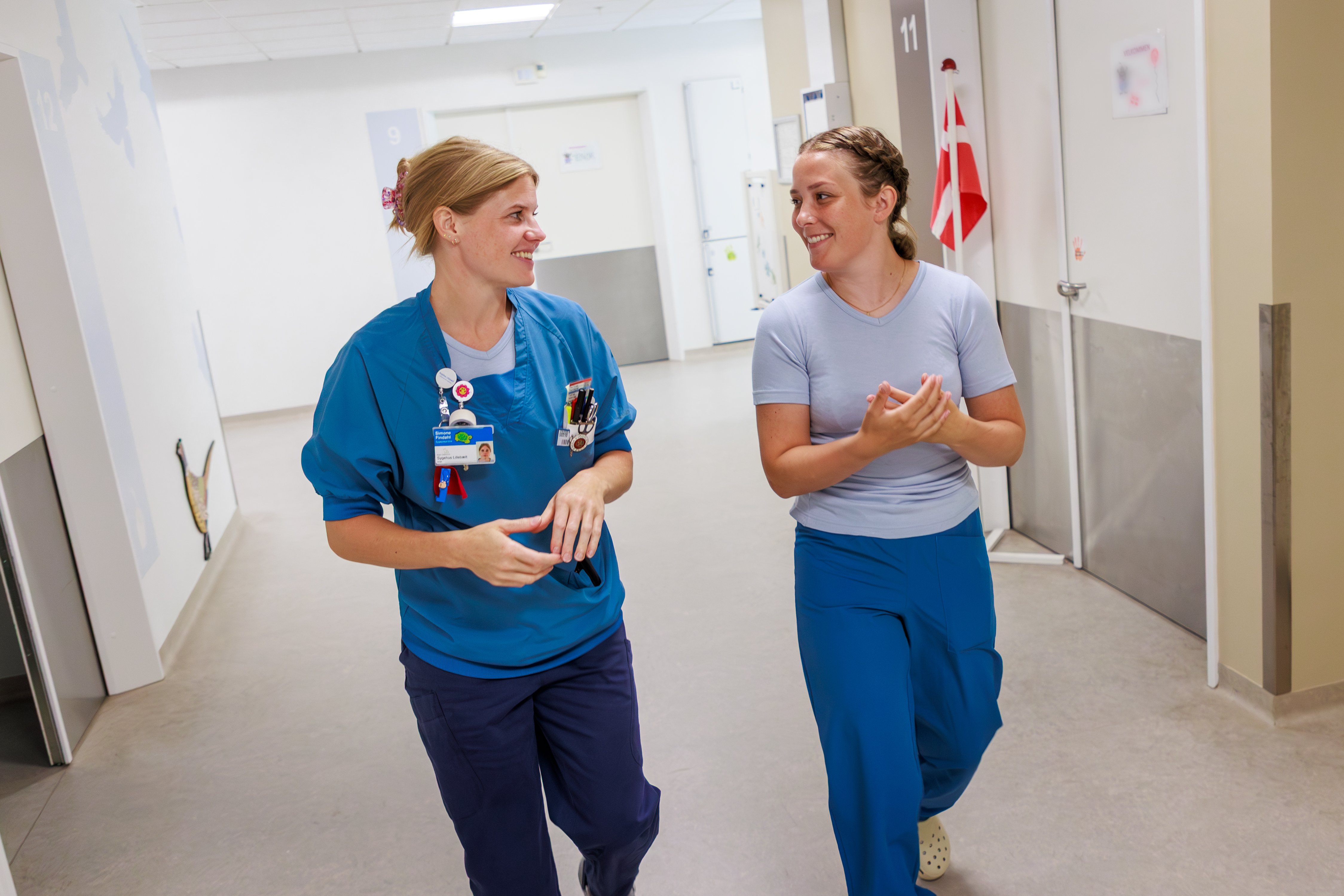 To kvindelige sygeplejersker går smilende på sygehusgang